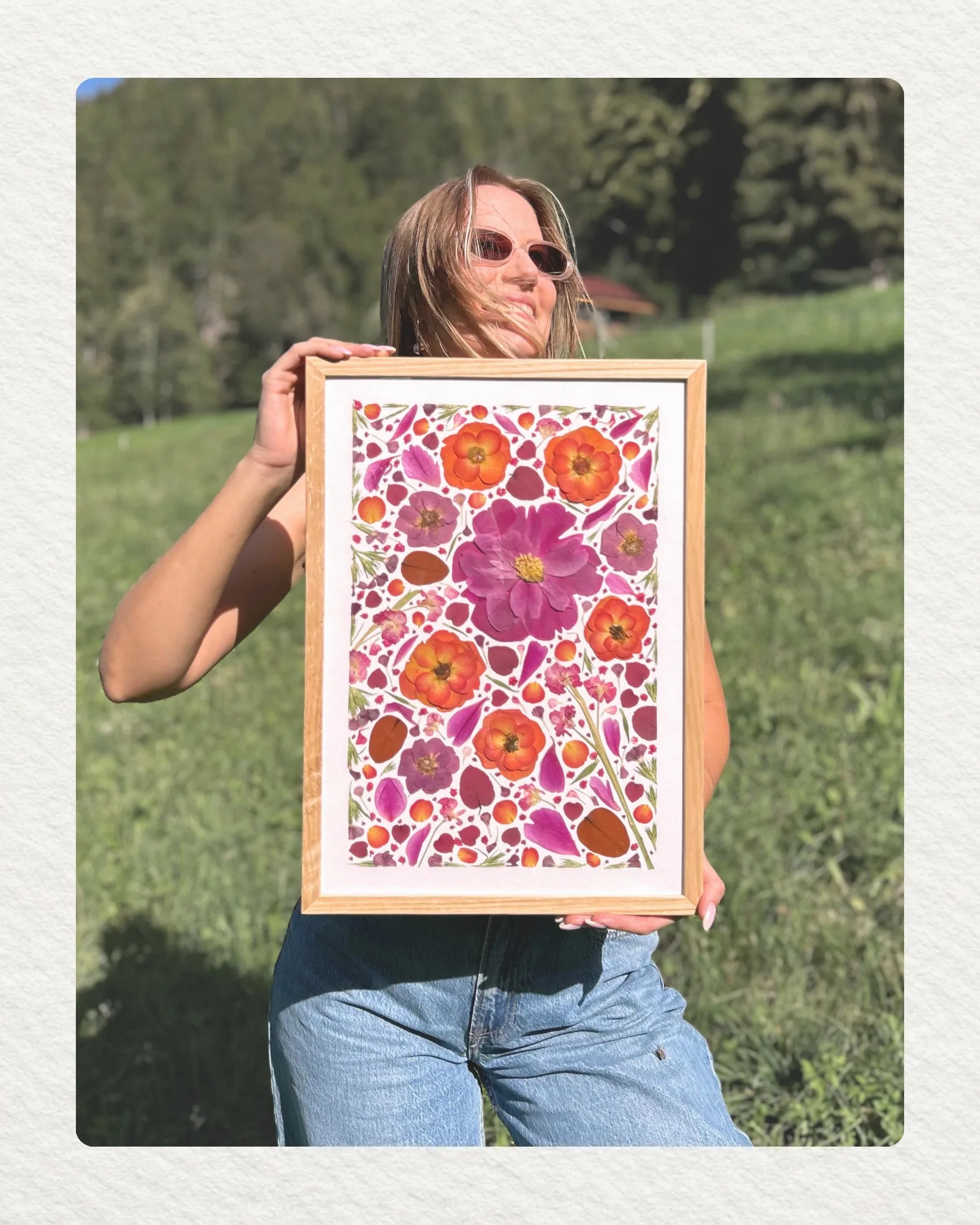 Céline présentant un tableau de fleurs pressées rose et orange devant un paysage valaisan