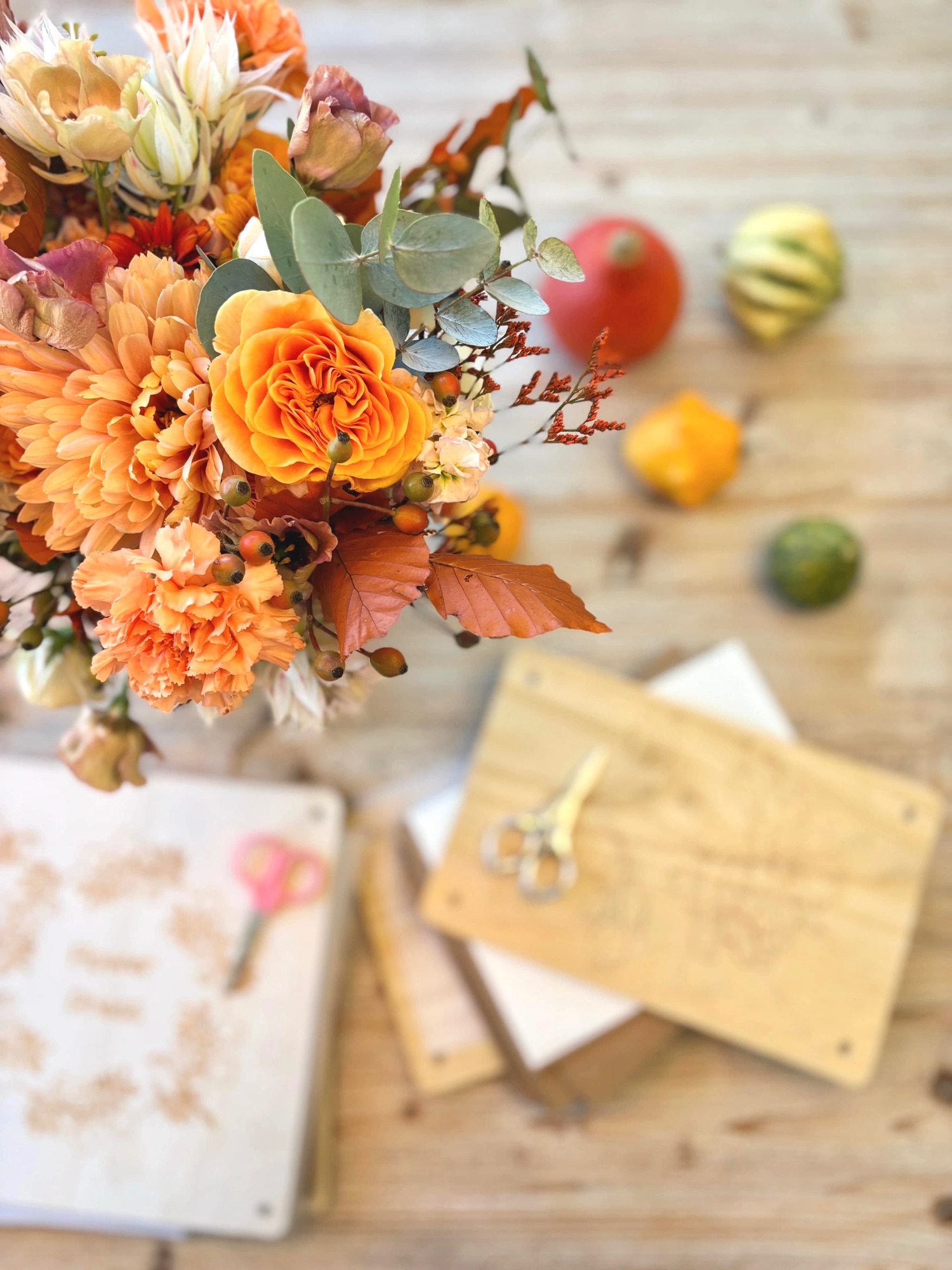 Bouquet de mariée aux tons orange et cuivre posé sur la table d'atelier de Studio Florae à Sion